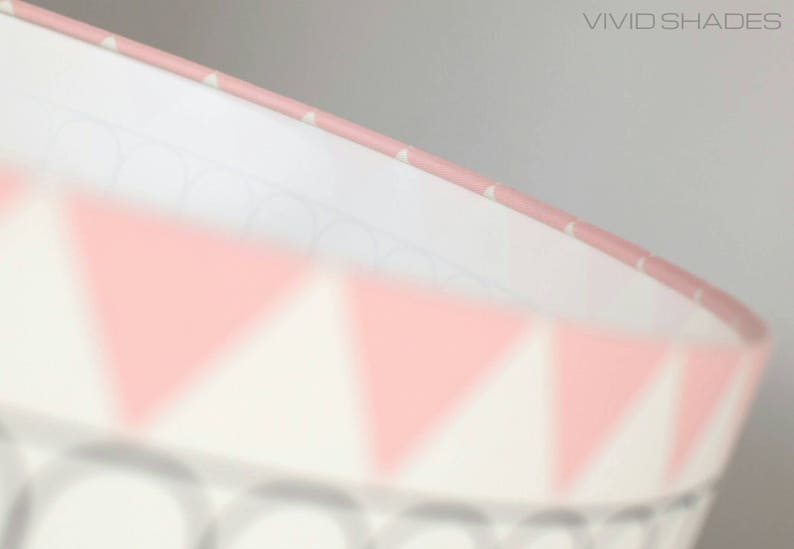 May include: A pink and white lampshade with a geometric pattern of triangles. The lampshade is made of fabric and has a white lining.