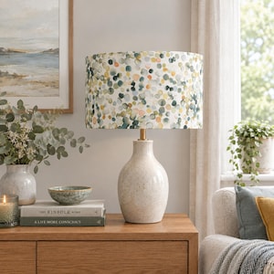 May include: A table lamp with a speckled, off-white ceramic base and a cylindrical fabric lampshade featuring a multicolored pattern of small, overlapping watercolor-style dots in shades of green, yellow, orange, and blue on a white background.