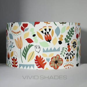 May include: A white cylindrical lampshade with a colorful floral pattern. The pattern features red, orange, yellow, green, and blue flowers and leaves. The lampshade has the text "VIVID SHADES" printed on the bottom.