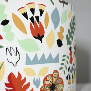 May include: A white lampshade with a colorful floral pattern. The pattern features red, orange, yellow, green, and blue flowers and leaves. The lampshade has the text "VIVID SHADES" printed on the bottom.