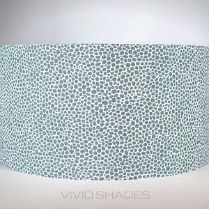 May include: A light blue lampshade with a white polka dot pattern. The lampshade is cylindrical and has a smooth surface.