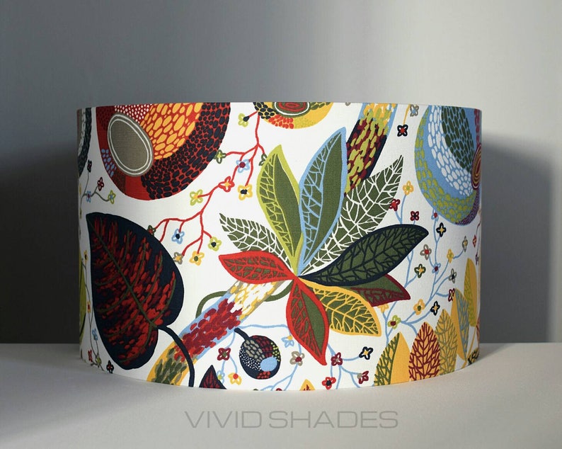 May include: A white lampshade with a colorful floral pattern featuring red, green, yellow, and blue leaves. The lampshade has a white background with a repeating pattern of stylized leaves and flowers.