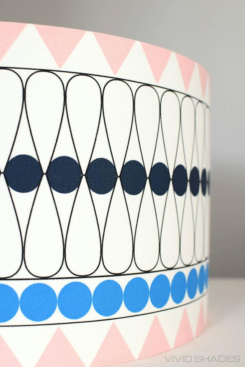 May include: A white lampshade with a geometric pattern of black and blue circles and teardrop shapes. The bottom of the lampshade has a pink and white triangle pattern.
