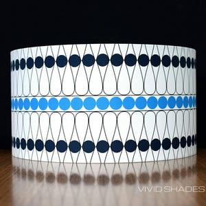 May include: A white lampshade with a geometric pattern of black and blue circles and teardrop shapes. The pattern is repeated around the lampshade.