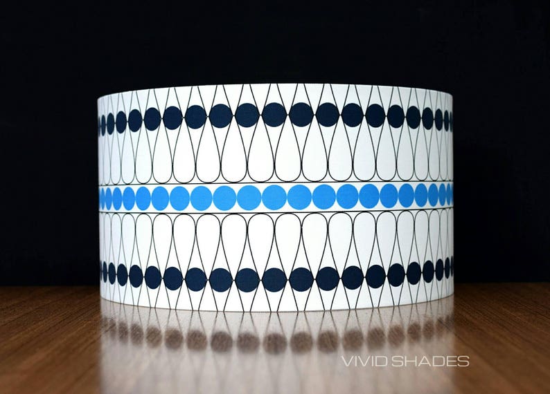 May include: A white lampshade with a geometric pattern of black and blue circles and teardrop shapes. The pattern is repeated around the lampshade.