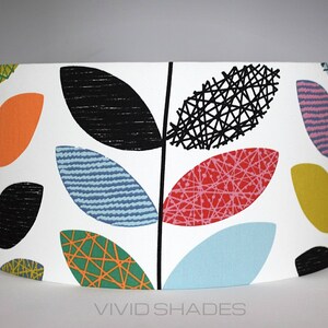 May include: A white lampshade with a colorful leaf pattern. The leaves are in shades of orange, red, green, blue, and black. The lampshade has a curved shape and is made of fabric.