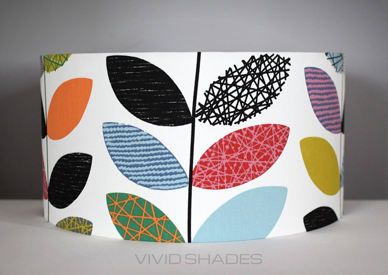 May include: A white lampshade with a colorful leaf pattern. The leaves are in shades of orange, red, green, blue, and black. The lampshade has a curved shape and is made of fabric.