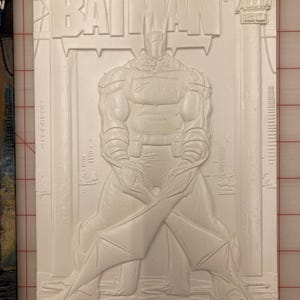 May include: A white relief sculpture of a Batman comic book cover. The title "ABSOLUTE BATMAN" is prominently displayed, with the DC Comics logo visible. The artwork depicts Batman in a dynamic pose.