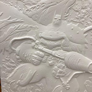 May include: A white relief sculpture depicting Batman holding a weapon. The artwork features detailed textures and a dynamic composition, showcasing the superhero in action. The background includes stylized elements.