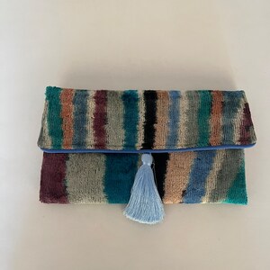 May include: A colorful striped clutch with a blue tassel. The clutch is made of a soft, textured fabric.