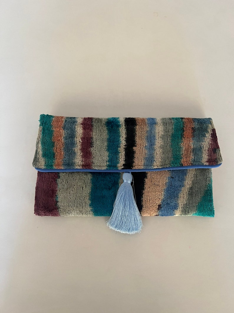 May include: A colorful striped clutch with a blue tassel. The clutch is made of a soft, textured fabric.