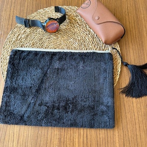 Op de afbeelding: Een zwarte ritszak met een kwast, een zwart horloge met een bruine wijzerplaat en een bruin leren zonnebril etui.