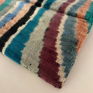 May include: A colorful striped clutch bag with a blue tassel. The bag is made of a soft, textured fabric.