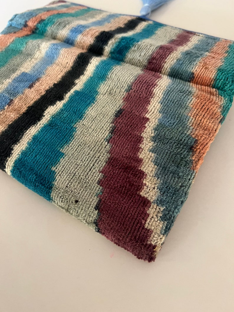 May include: A colorful striped clutch bag with a blue tassel. The bag is made of a soft, textured fabric.