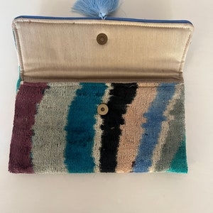 May include: A blue and white striped clutch with a blue tassel. The clutch has a fabric lining and a snap closure.