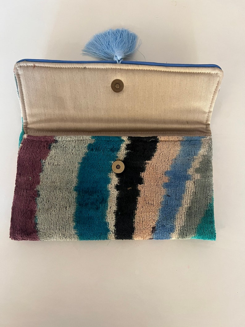 May include: A blue and white striped clutch with a blue tassel. The clutch has a fabric lining and a snap closure.