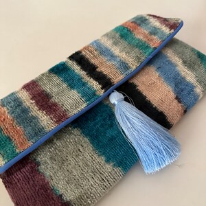 May include: A colorful striped clutch purse with a blue tassel. The clutch is made of a soft, textured fabric and has a blue trim.