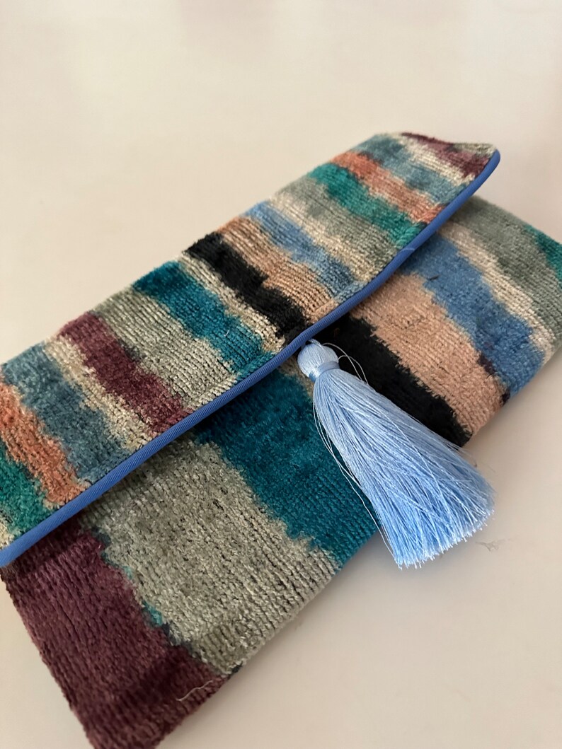 May include: A colorful striped clutch purse with a blue tassel. The clutch is made of a soft, textured fabric and has a blue trim.