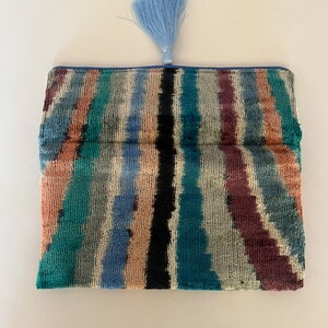 May include: A blue and green striped clutch with a blue tassel. The clutch is made of a soft, velvety fabric.