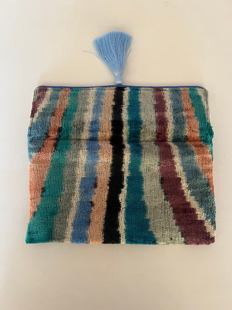 May include: A blue and green striped clutch with a blue tassel. The clutch is made of a soft, velvety fabric.