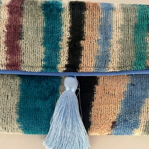May include: A blue and brown striped clutch with a light blue tassel.