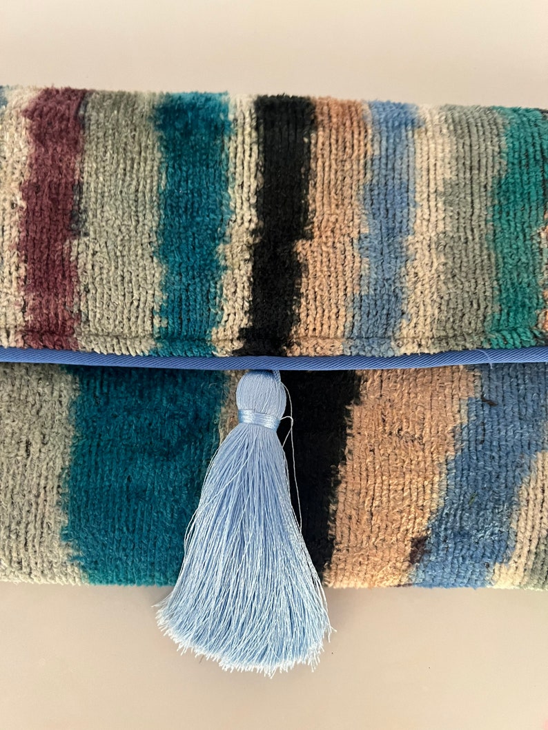 May include: A blue and brown striped clutch with a light blue tassel.