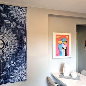 May include: A navy blue and white tie-dye textile hanging on a wall. The textile features a repeating pattern of floral and circular designs. A framed art print and decorative vases are also visible.