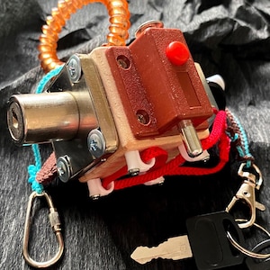 Puede incluir: Primer plano de una cerradura plateada y roja con una llave adjunta. La cerradura tiene un botón rojo y una cerradura plateada. La cerradura está unida a un cordón rojo y blanco.