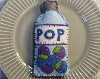 May include: A felt ornament shaped like a blue bottle with the word "POP" on the front. The bottle is decorated with purple and green felt berries.