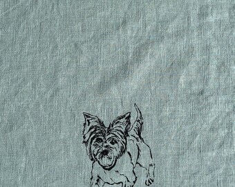 May include: A light blue textile features a black line drawing of a Yorkshire Terrier dog. The dog is depicted in a running pose, with its ears perked up and tail curved. The textile has a textured appearance.