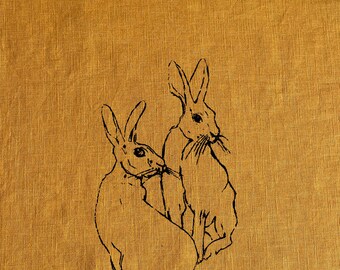 May include: Two black line drawings of rabbits on a yellow linen background. The rabbits are facing each other and appear to be interacting.