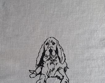 May include: Black and white line drawing of a cocker spaniel dog sitting on a gray linen background.