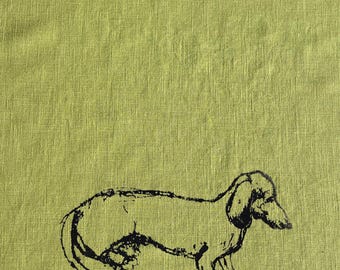 May include: A black and white line drawing of a dachshund dog on a green linen background.