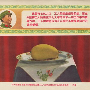 May include: A propaganda poster featuring a portrait of Mao Zedong, the former Chairman of the Communist Party of China, with a caption in Chinese that reads: "Our country has 700 million people, the working class is the leading class, we must fully bring into play the leading role of the working class in the Cultural Revolution and all work. The working class should also constantly raise its political consciousness." The poster also features a mango on a plate, which is a gift from Mao Zedong to the workers.