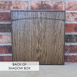 May include: The back of a dark brown wooden shadow box with a wire hanger attached.