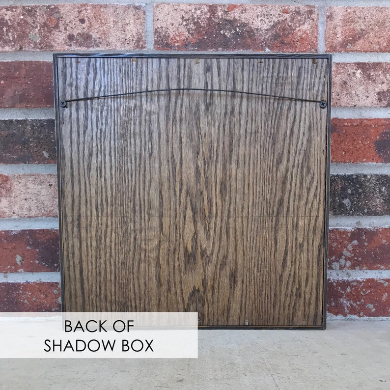May include: The back of a dark brown wooden shadow box with a wire hanger attached.