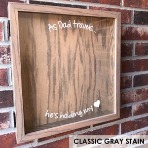 May include: A wooden shadow box with a glass front. The box has a white inscription that reads "As Dad travels... he's holding my heart". The box is stained a classic gray color.