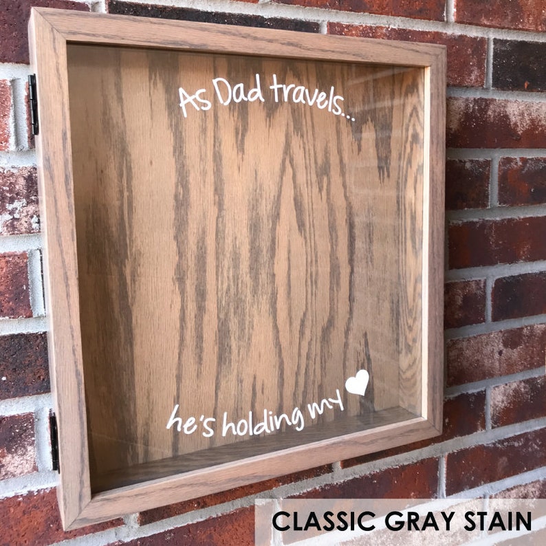 May include: A wooden shadow box with a glass front. The box has a white inscription that reads "As Dad travels... he's holding my heart". The box is stained a classic gray color.