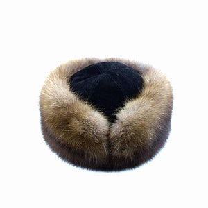 Puede incluir: Un sombrero de gamuza negro con ribete de piel marrón. El sombrero es redondo y tiene una parte superior plana.