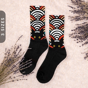 May include: A pair of black socks with a colorful geometric pattern of overlapping semi-circles. The pattern features black, white, orange, red, and blue colors. The socks have a black cat face design on the front.