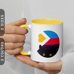 May include: White ceramic mug with a yellow rim. The mug features a black cat with yellow eyes and a colorful geometric design behind it. The design includes a yellow heart.