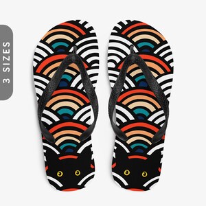 May include: Black flip flops with a colourful geometric pattern of overlapping semi-circles. A black cat face with yellow eyes is visible in the centre of the pattern.