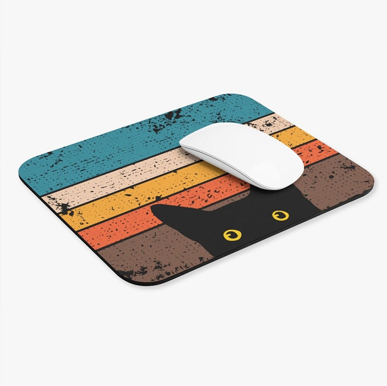 May include: A black cat with yellow eyes peeks over a retro-style striped mouse pad with a white computer mouse on top. The mouse pad has a distressed, vintage look with faded colors.