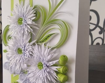 May include: A white card with a green and white paper flower arrangement. The flowers are made of curled paper and have a 3D effect. The card is blank and ready for a message.