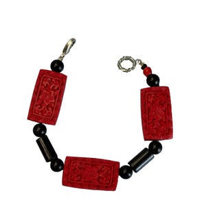 May include: A red and black bracelet with carved red rectangular beads and black round beads. The bracelet has a silver clasp.