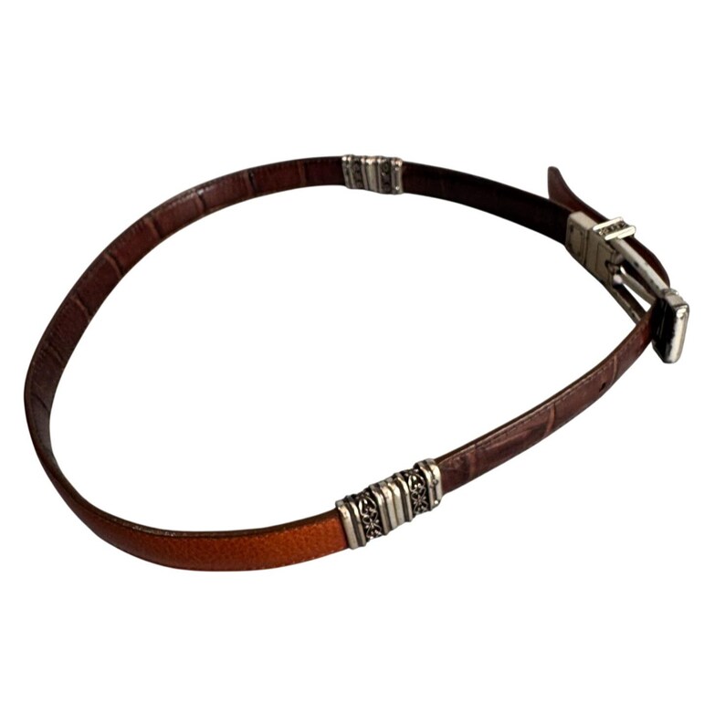 Peut inclure: Une ceinture en cuir marron avec un motif textur&eacute; gaufr&eacute; fa&ccedil;on crocodile, agr&eacute;ment&eacute;e de deux segments d&eacute;coratifs en m&eacute;tal argent&eacute; et d'une boucle en m&eacute;tal argent&eacute; assortie avec un syst&egrave;me de fermeture &agrave; ardillon.