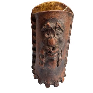 Peut inclure: Un vase en céramique marron fait à la main avec un visage sculpté. Le vase a une surface texturée et un bord festonné. Le visage présente une moustache, une barbe et une expression fantaisiste. L'intérieur est de couleur marron clair.