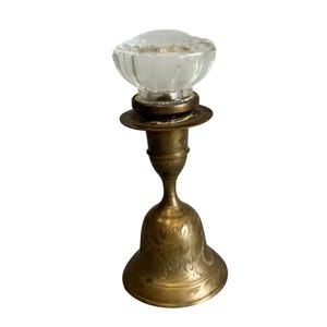 Könnte beinhalten: Ein Vintage-Messing-Kerzenhalter mit einer durchsichtigen Glasoberseite. Der Kerzenhalter hat einen glockenförmigen Sockel mit geätzten floralen Designs. Die Glasoberseite hat eine klare, gerippte Schalenform. Der Kerzenhalter hat eine warme Messingfarbe.