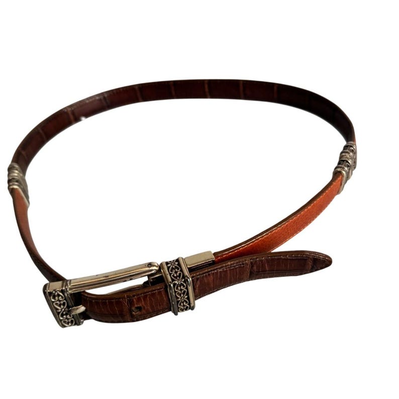 Peut inclure: Une ceinture en cuir marron avec un motif textur&eacute; gaufr&eacute; fa&ccedil;on crocodile. La ceinture pr&eacute;sente une boucle en m&eacute;tal argent&eacute; et deux passants d&eacute;coratifs en m&eacute;tal argent&eacute;, chacun orn&eacute; d'un motif complexe en filigrane.