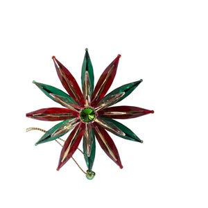 May include: A starburst-shaped Christmas ornament with alternating red and green petals. The ornament has gold accents, a green gem centre, and a gold string for hanging. The design resembles a flower, perfect for festive decorations.